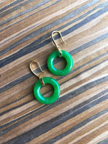 A pair of vivid green jade circle earrings with 18k gold hooks on the top of a wooden table