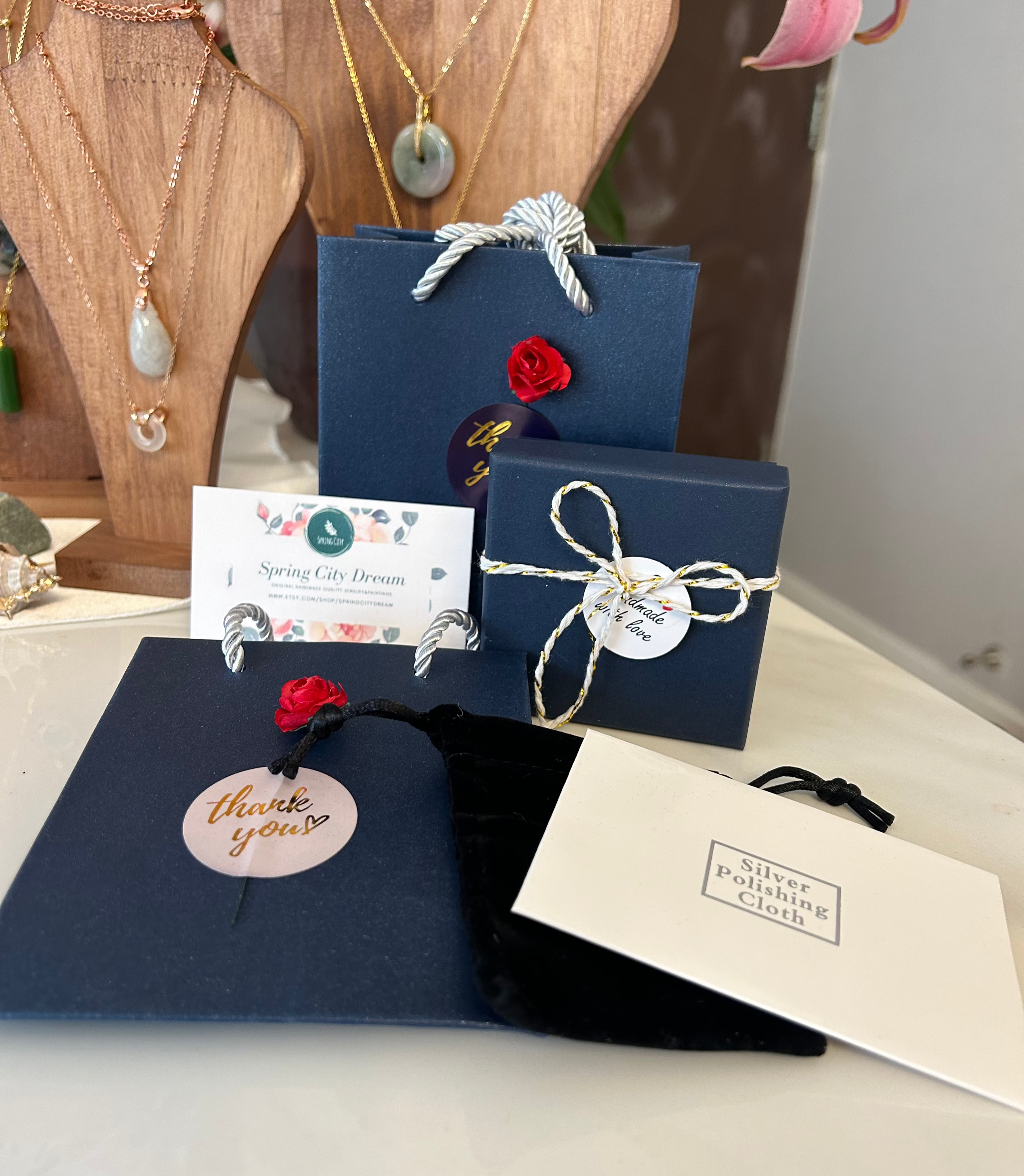 Set of blue gift boxes with decorative ribbons, black felt jewelry bag, white silver polish cloth, and a name cards on a table.
