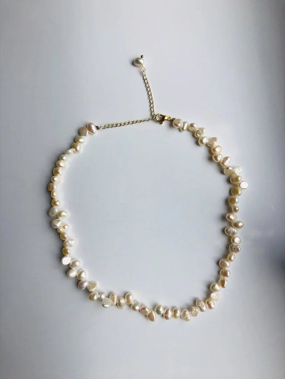 An irregular natural pearl necklace with gold-filled pearl beads. The necklace is white and gold in color, with an adjustable chain.
