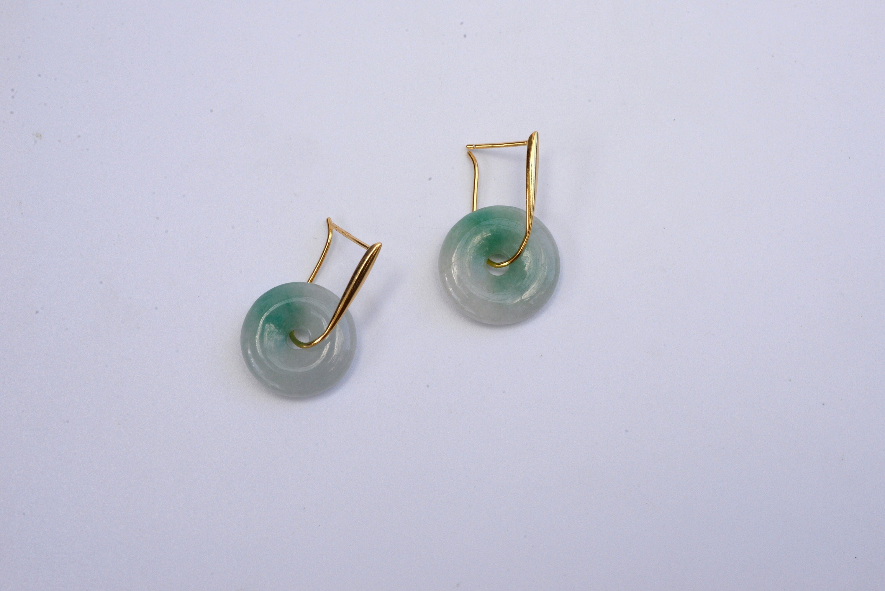 A pair of gold hanging jade donut earrings with a green and white color scheme against a white background.
