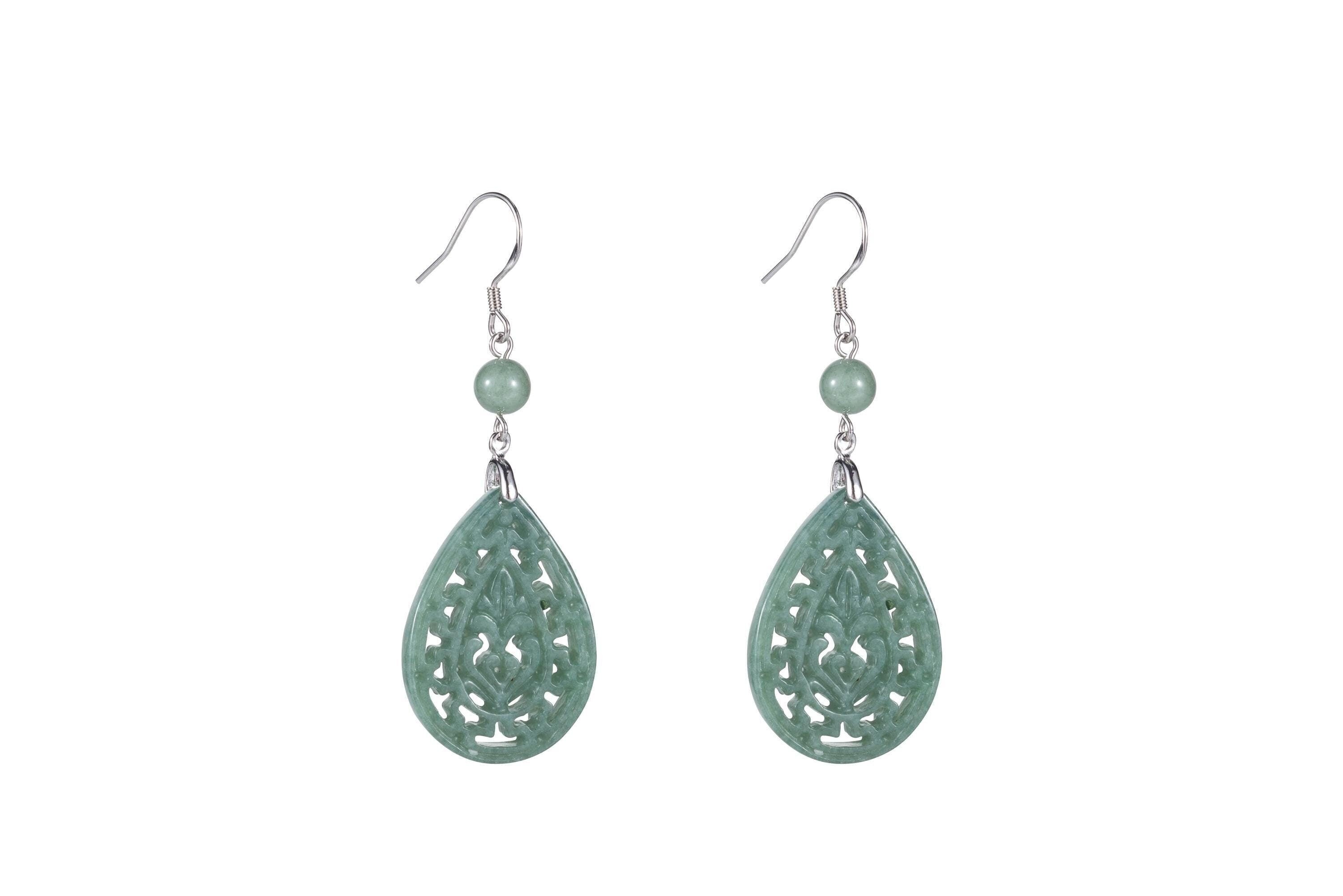 A pair of light green jade teardrop earrings with intricate cut-out patterns, suspended from silver hooks.