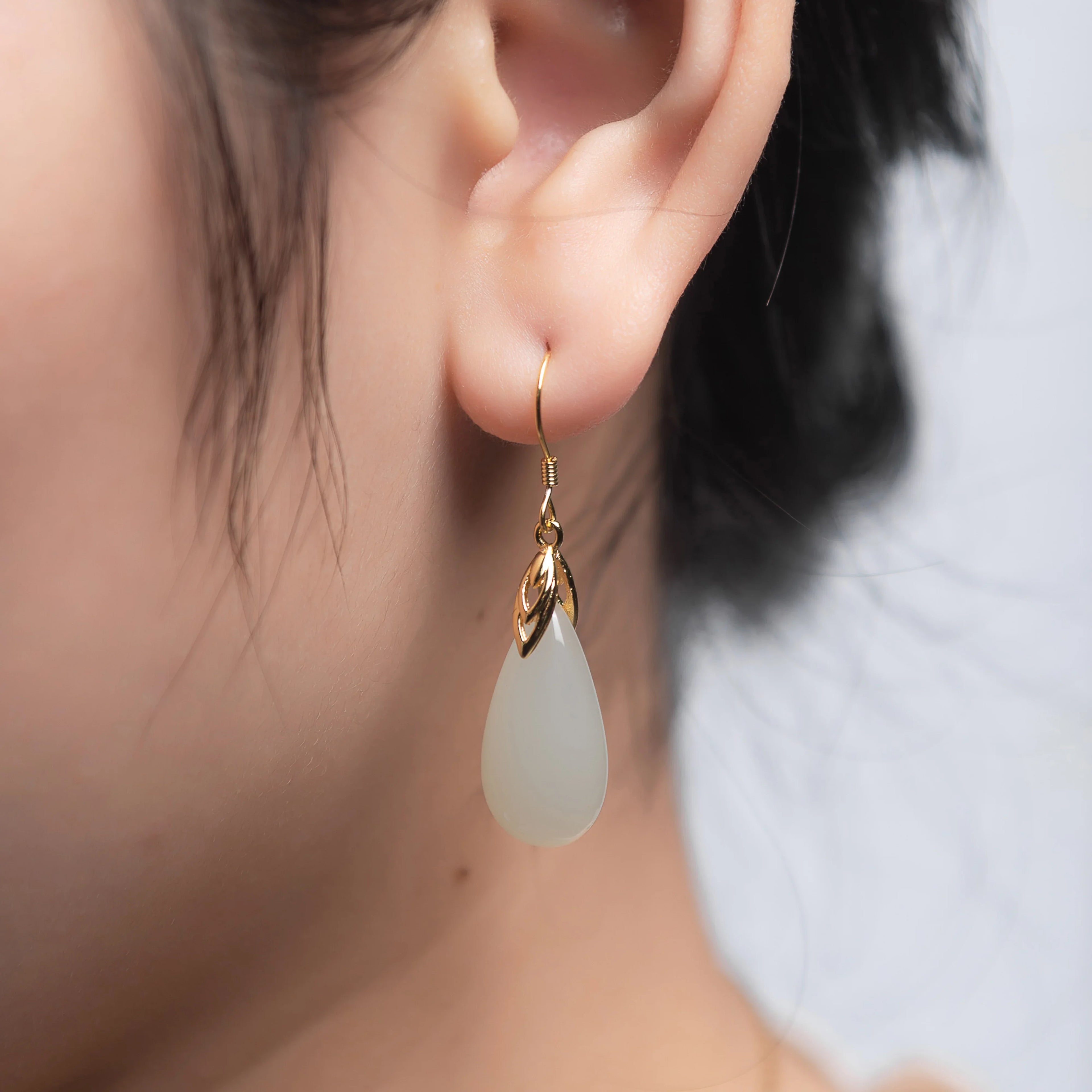 A girl wearing Elegant white jade earrings with polished gold hooks in classic drop design
