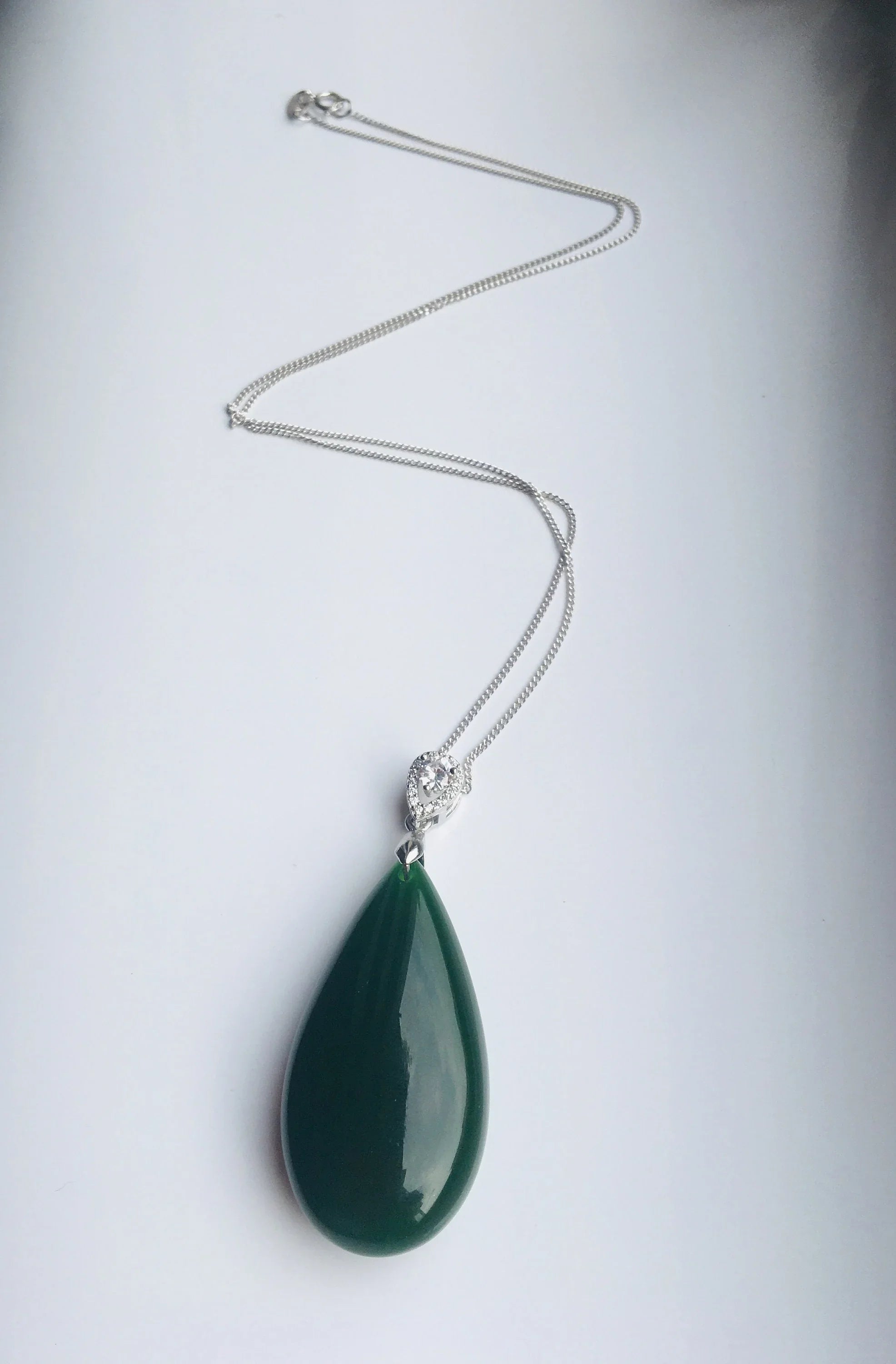 Green teardrop pendant on a silver chain against a white background