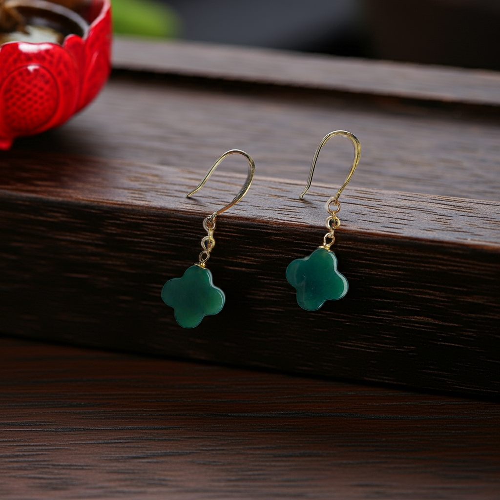Clover-shaped green jade earrings on a dark wooden table with red decorations