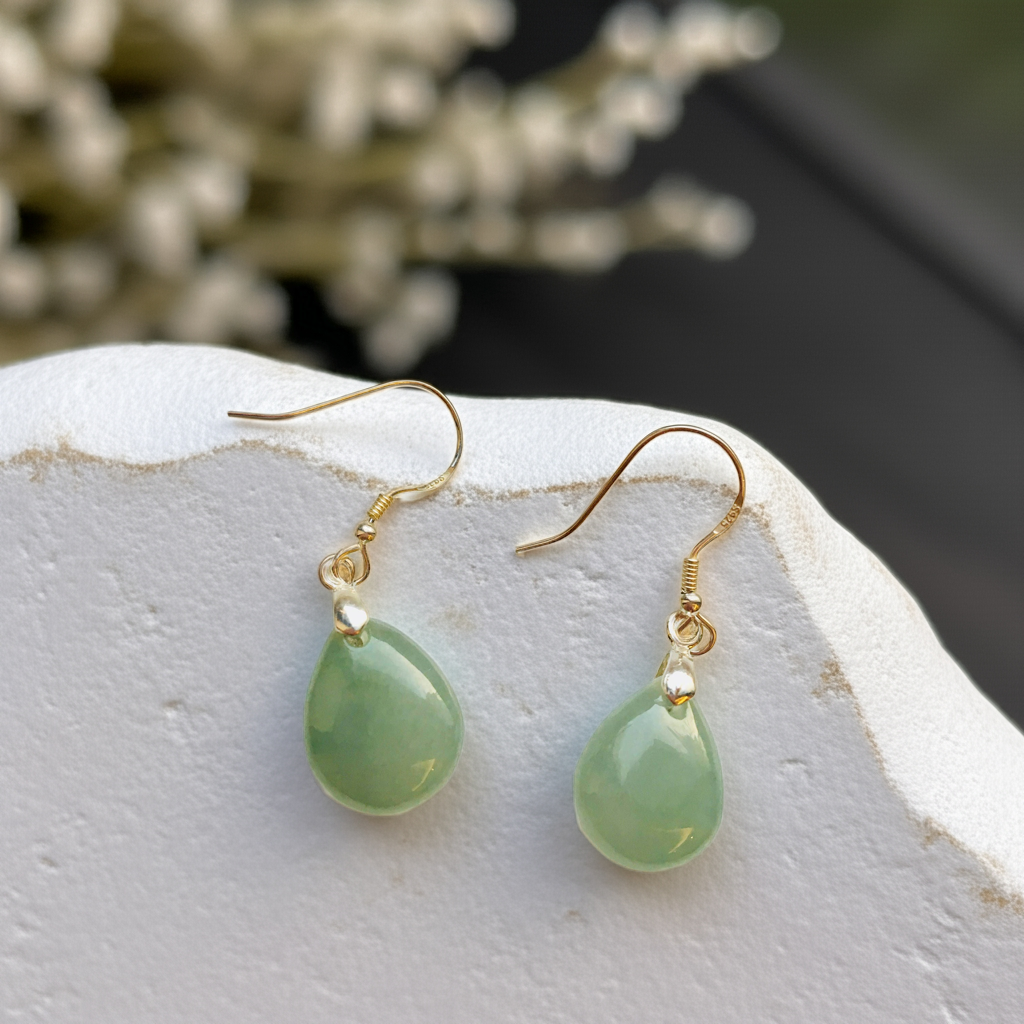 Green teardrop earrings with gold hooks on a light stone surface.