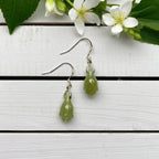 Green Jade Flower Bud Drop Earrings on a white wood table with white flower in the corner