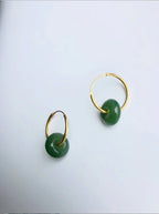 Gold hoop earrings with green round stones on a light gray background