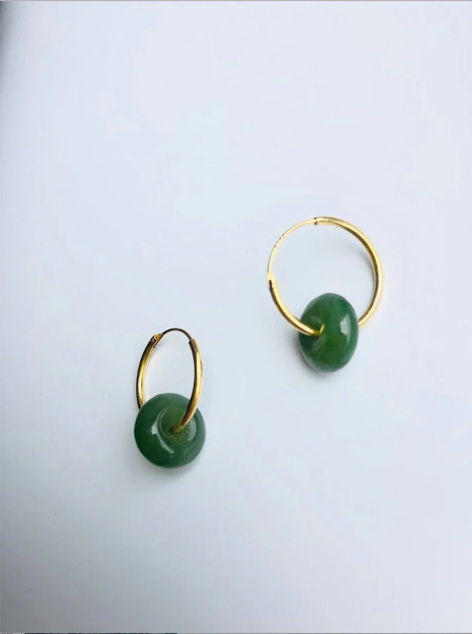 Gold hoop earrings with green round stones on a light gray background