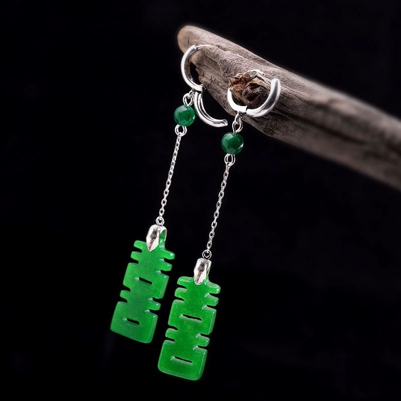 Green earrings with silver chains on a dark background