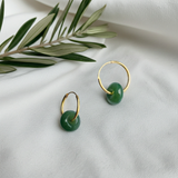 a pair of jade earrings with gold hoop on top of white fabric and olive leaves decoration