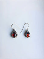 A pair of sterling silver teardrop earrings with red zircon gemstone drops and lace detailing, displayed against a white background.