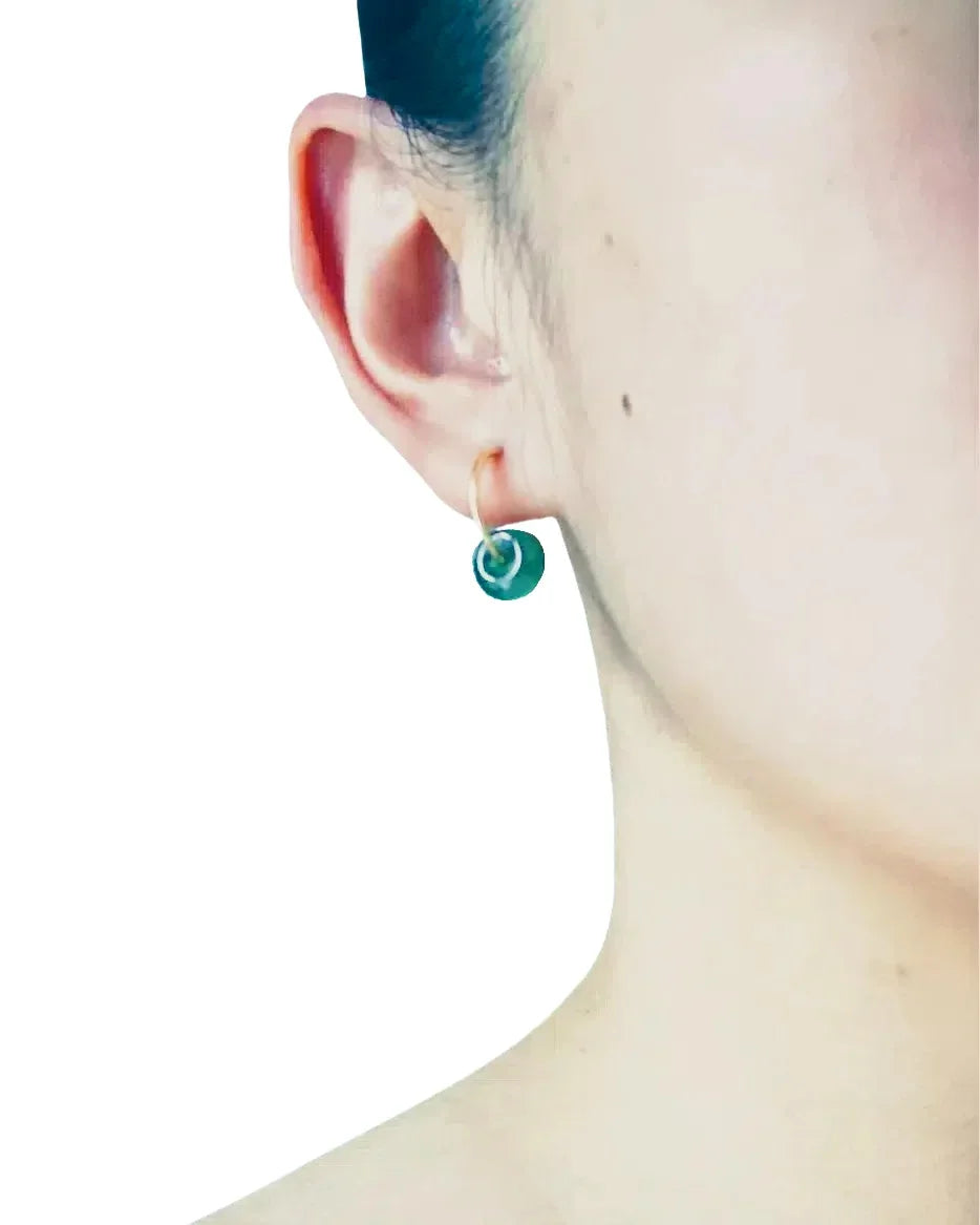 Close-up of an ear wearing a green earring on a white background