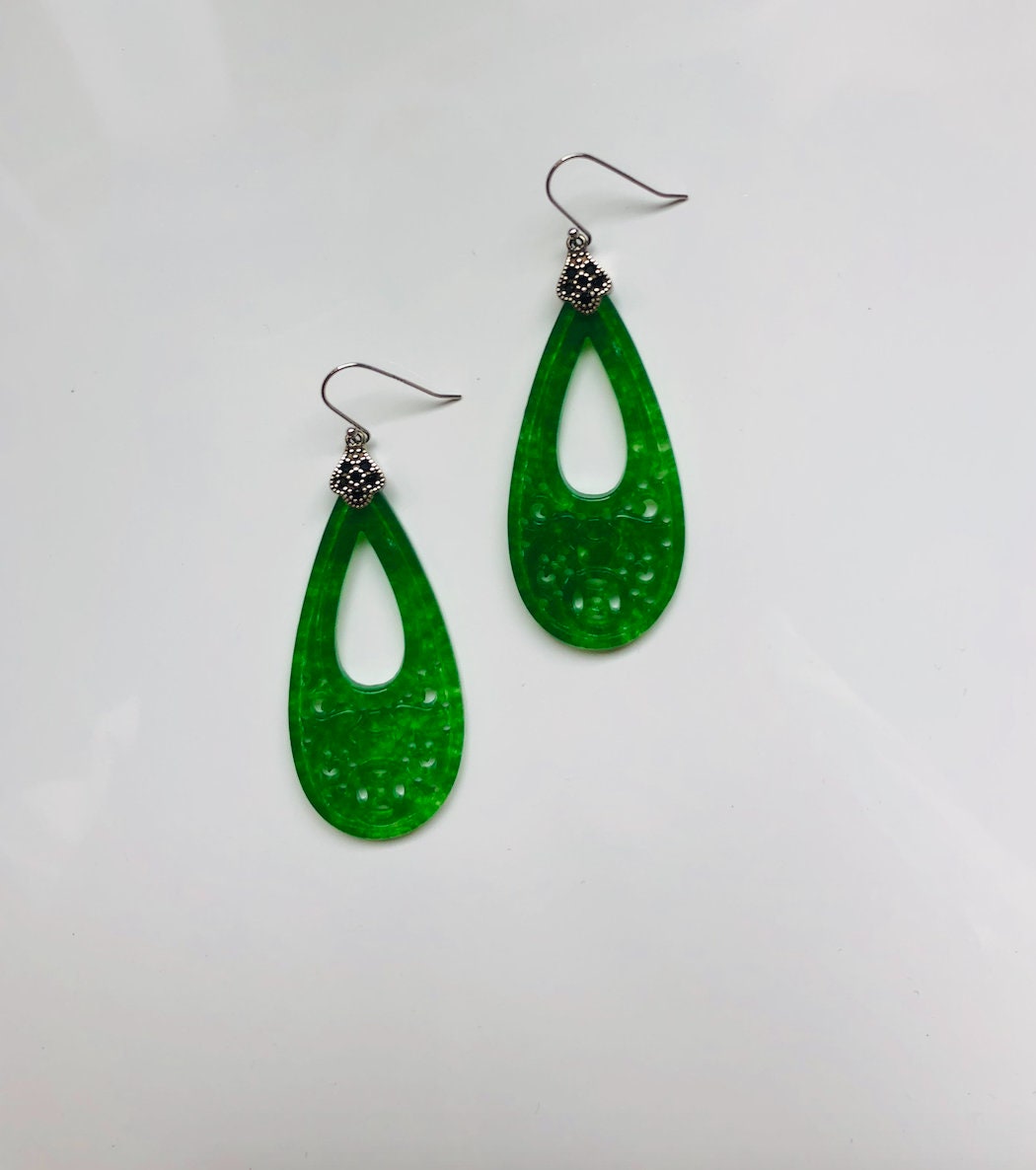 intricate carved jade teardrops with vintage silver setting under natural lighting