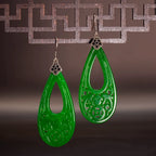 Green teardrop earrings with intricate designs on a dark background