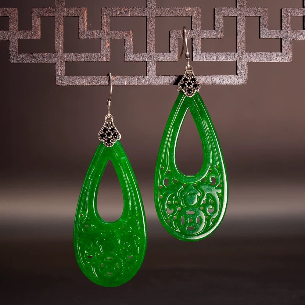 Green teardrop earrings with intricate designs on a dark background