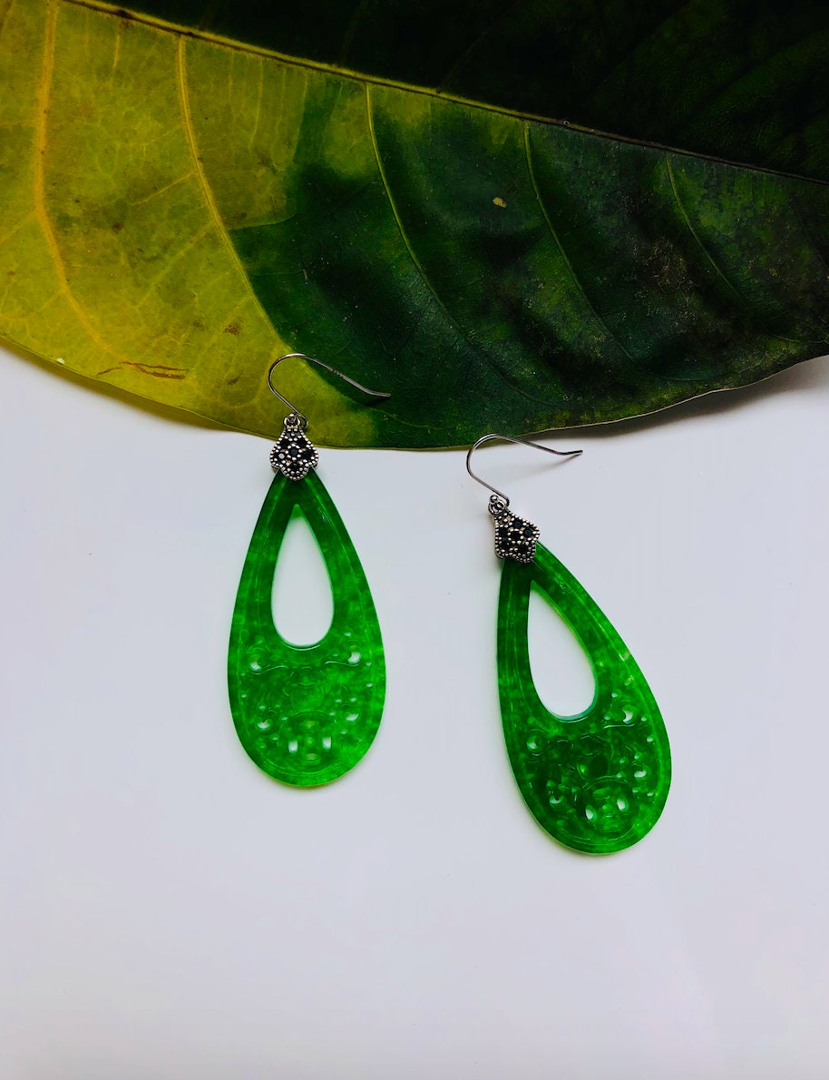 Carved jade and silver dangle earrings placed with a leaf