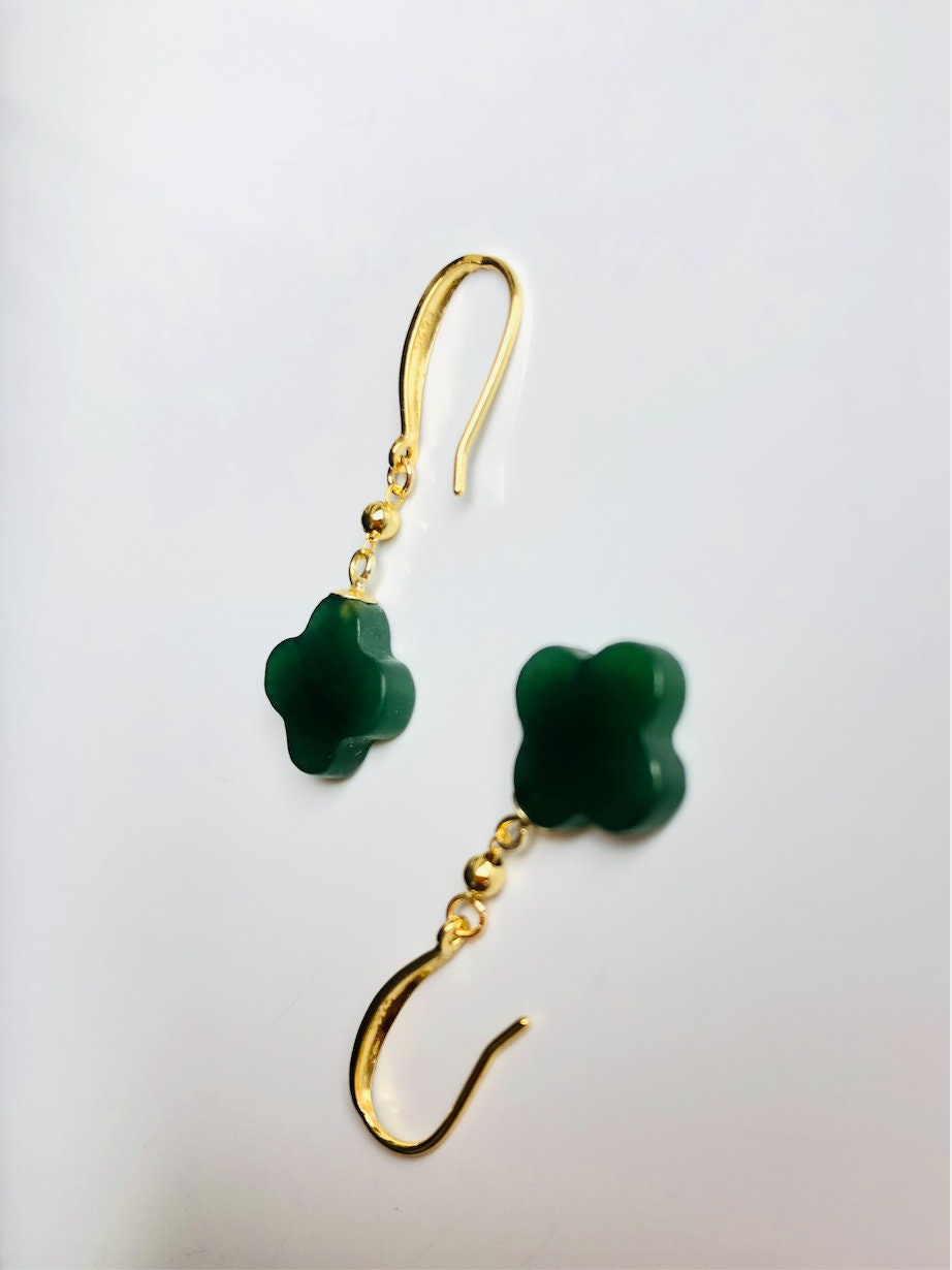 Side angle of clover-shaped gold earrings with dangling green jade charm

