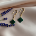 Clover-shaped green jade earrings on a soft silk fabric with lavender decorations