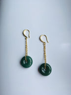 A pair of dark green jade donut earrings with gold-colored chains and hooks, displayed against a light background.