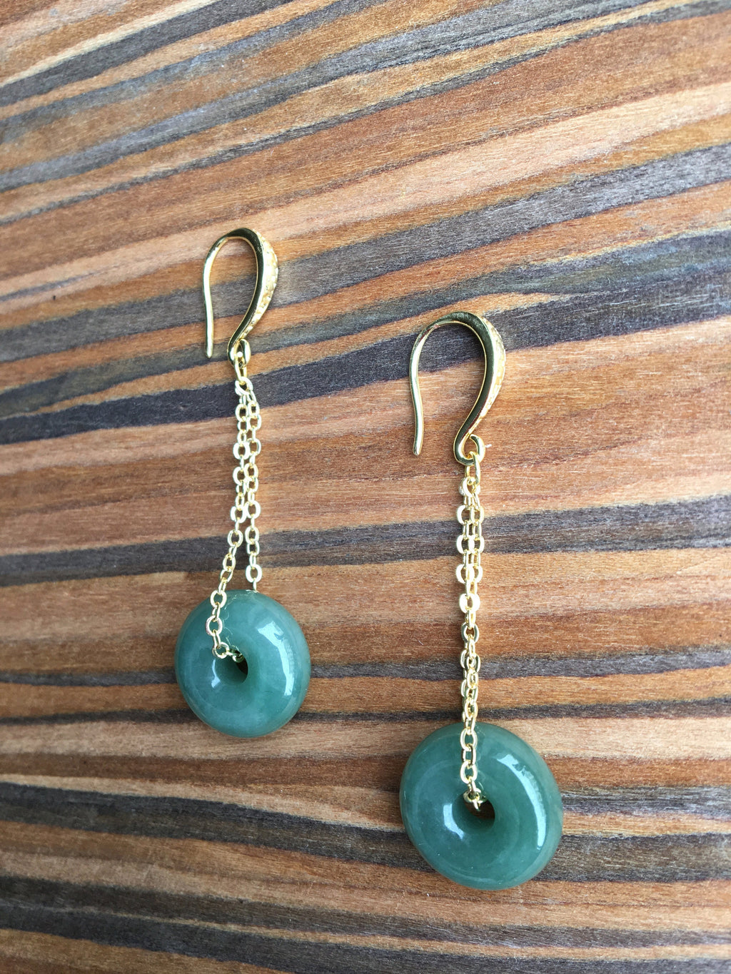  jade donut earrings showing smooth round surface and gold setting on a wood table