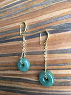  jade donut earrings showing smooth round surface and gold setting on a wood table