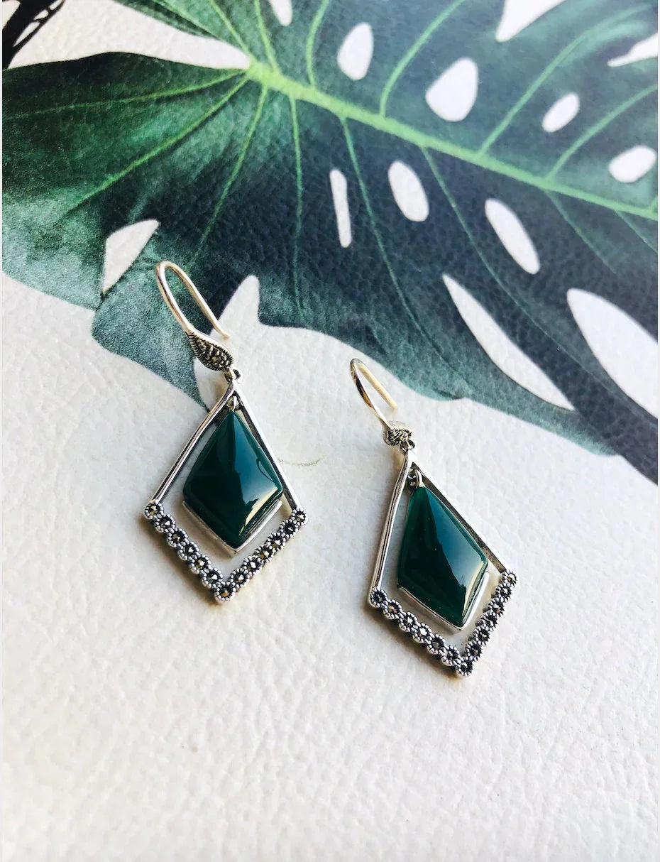 Front view of dark green diamond-shaped jade earrings with sterling silver hoops on leaf