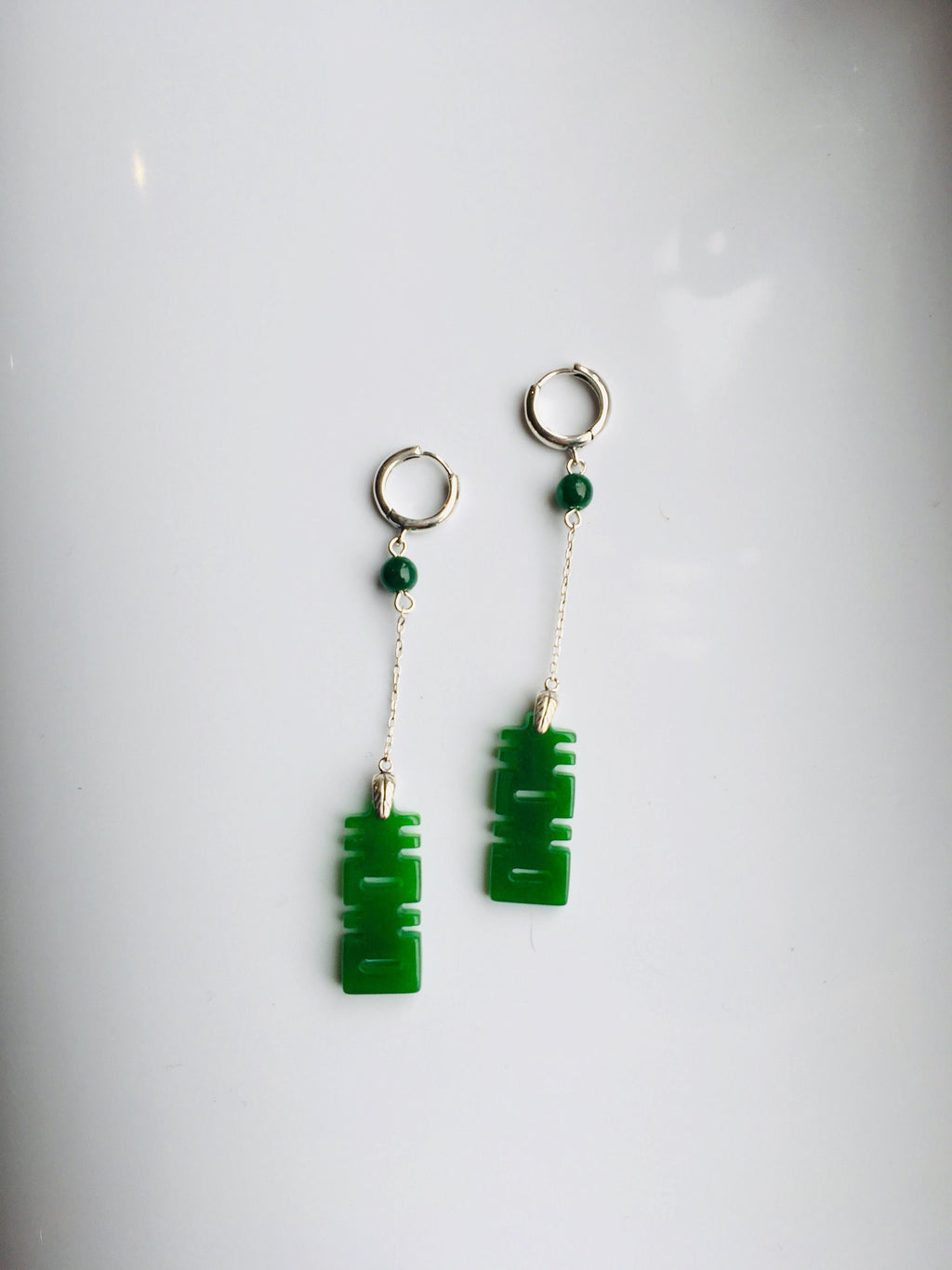 A pair of long dangle earrings featuring dark green jade characters attached to 925 sterling silver hooks.