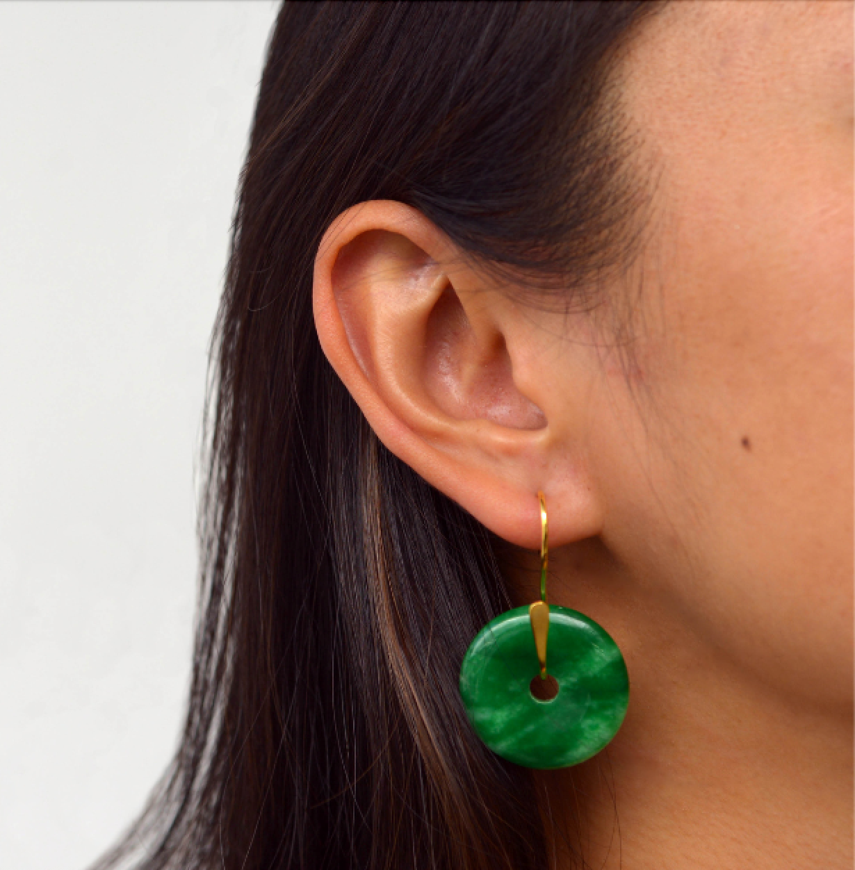 Close-up of a person wearing a green earring with a plain background