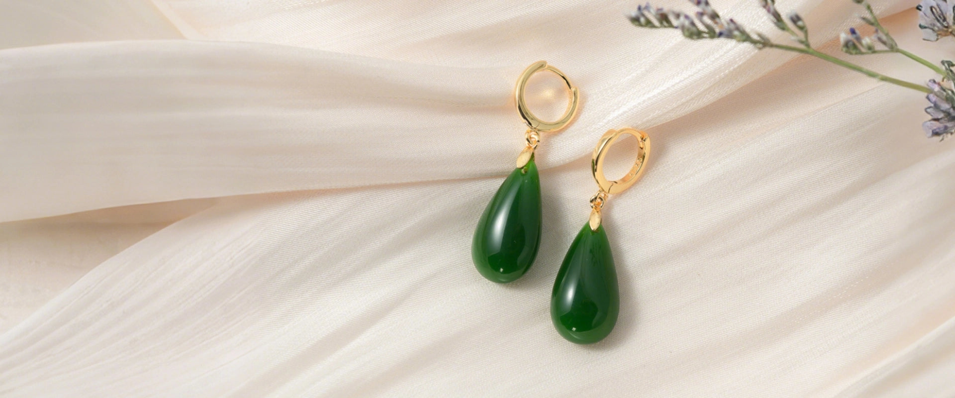 a pair of real green jade teardrop jewelry with golden hooks on a beige silk fabric 