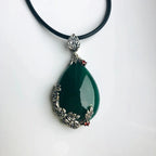 A dark green jade teardrop pendant necklace with silver floral designs on a black leather cord.
