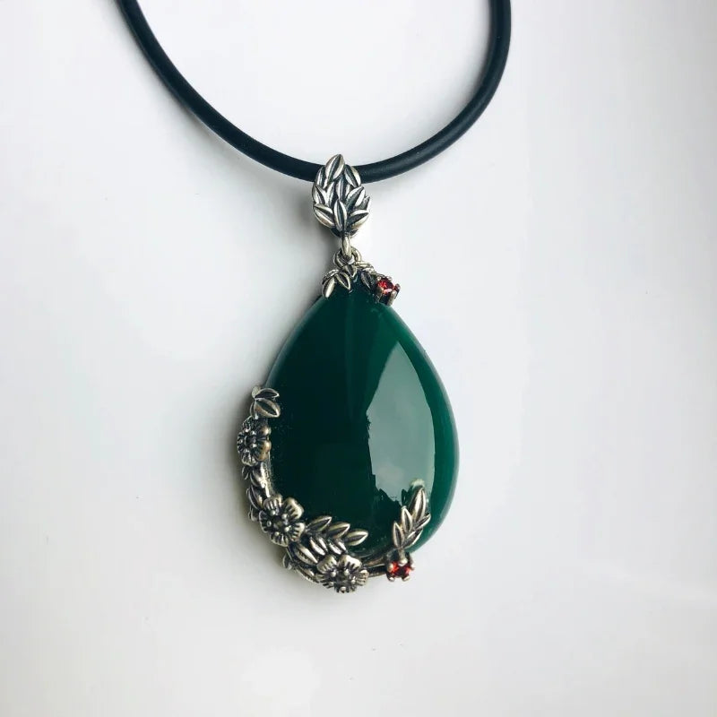 A dark green jade teardrop pendant necklace with silver floral designs on a black leather cord.