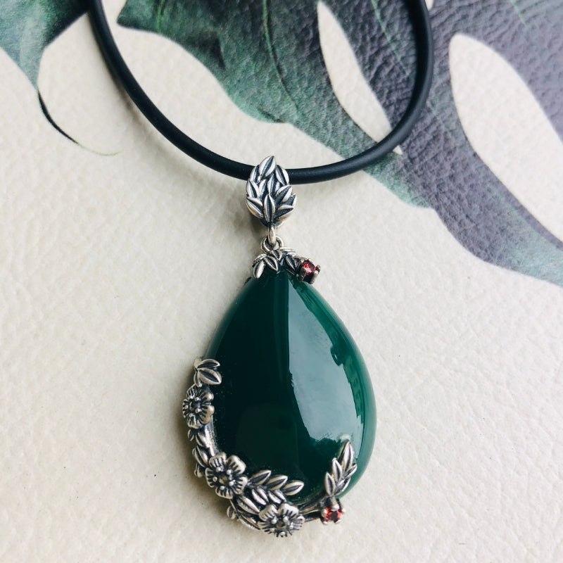 A dark green jade teardrop pendant necklace with silver floral designs on a black leather cord.