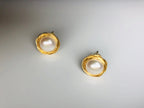 A pair of gold-filled wired pearl stud earrings placed on a white surface.