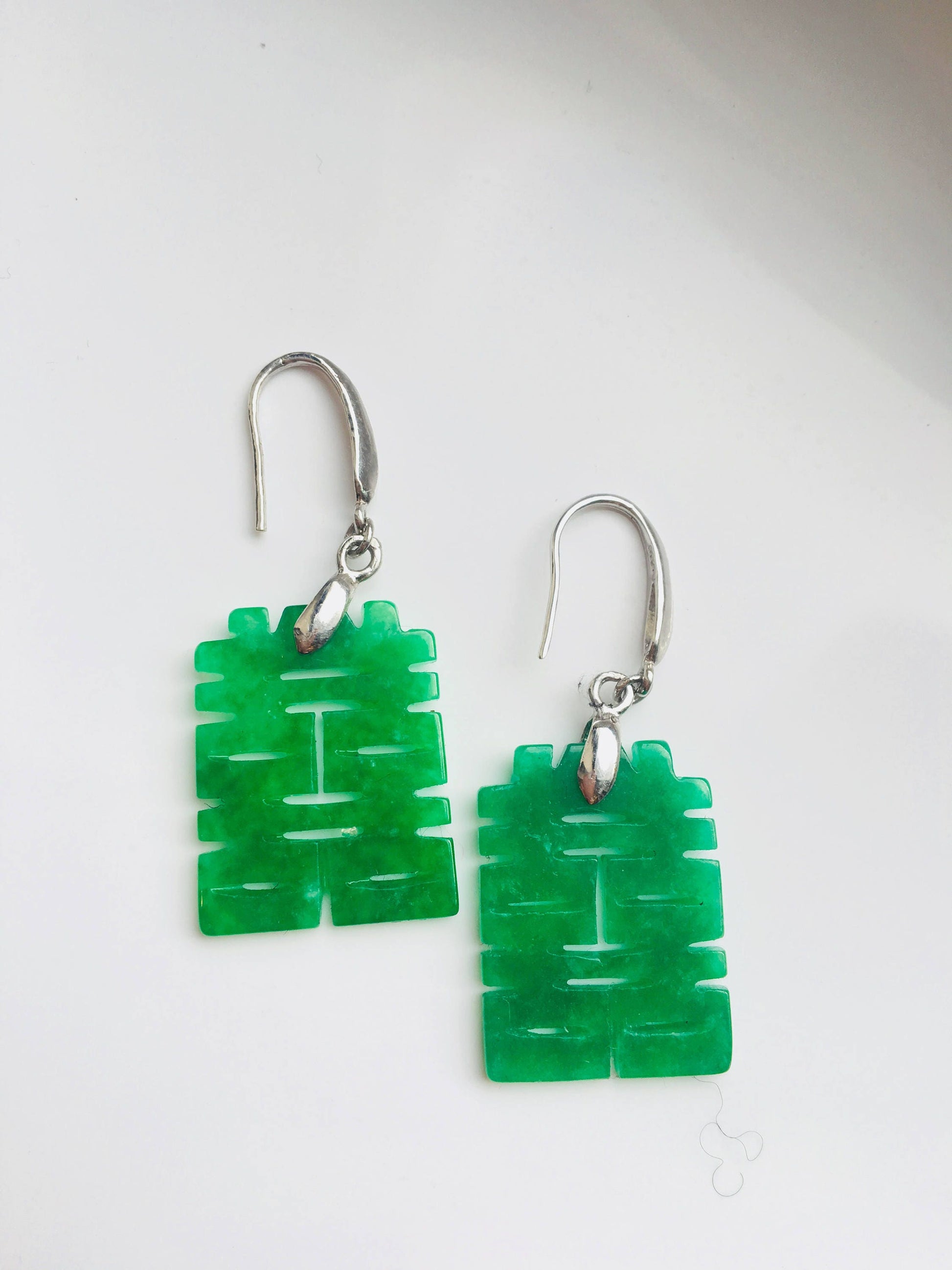 A pair of green jade dangle earrings with Chinese characters carved into the jade, hanging from silver hooks.