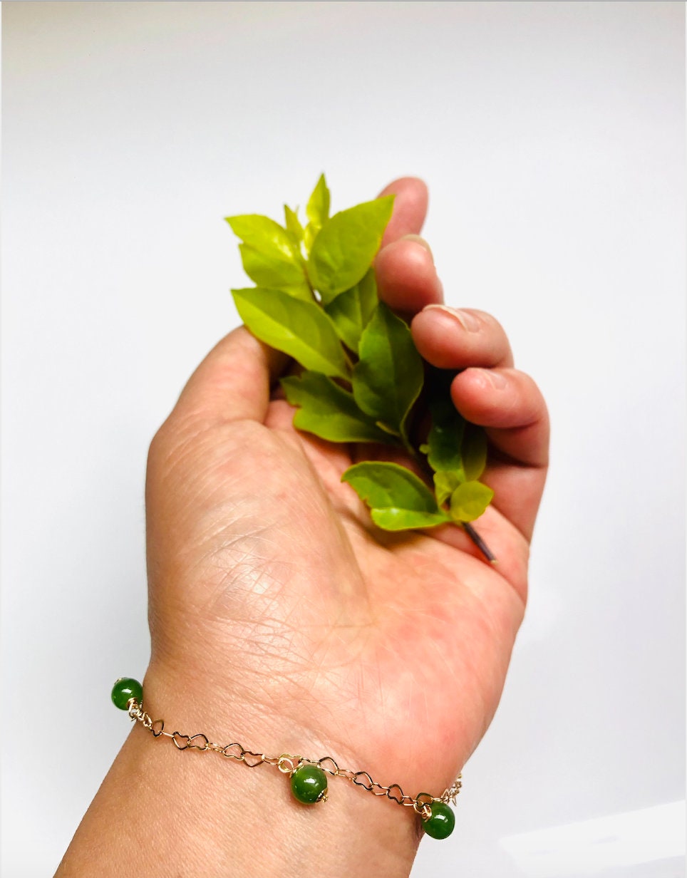 Model wearing dainty green jade bead bracelet with gold hearts

