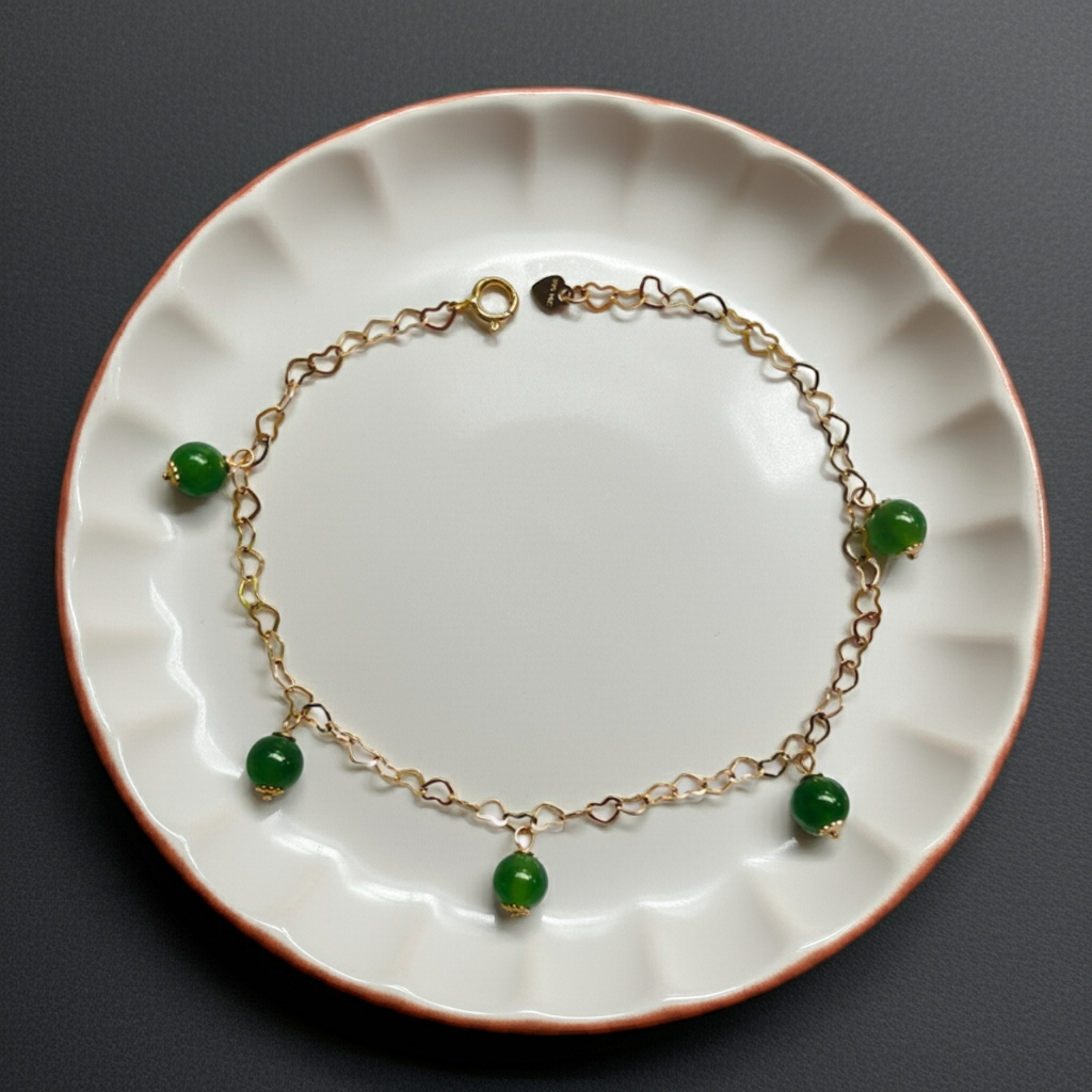 Front view of 14k gold filled bracelet with green jade beads and heart charms on a ceramic plate