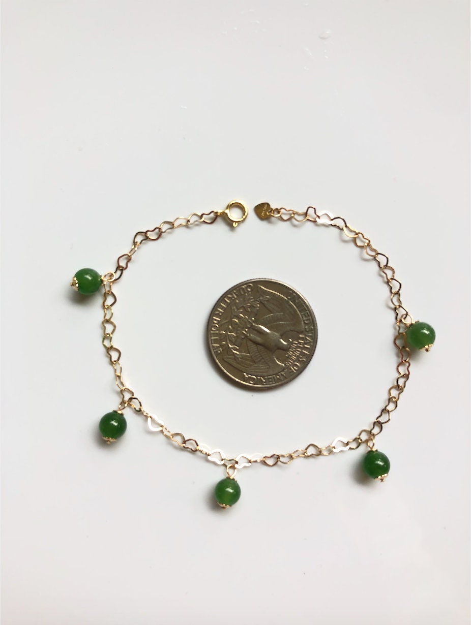 Adjustable jade bracelet with gold charms shown next to coin for size