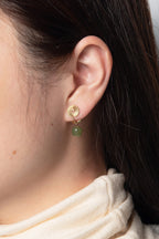 A model wearing a pair of green jade drop earrings with gold clip-on hooks.