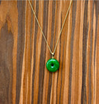 Front view of minimalist green jade donut necklace with 18k gold chain on wooden table