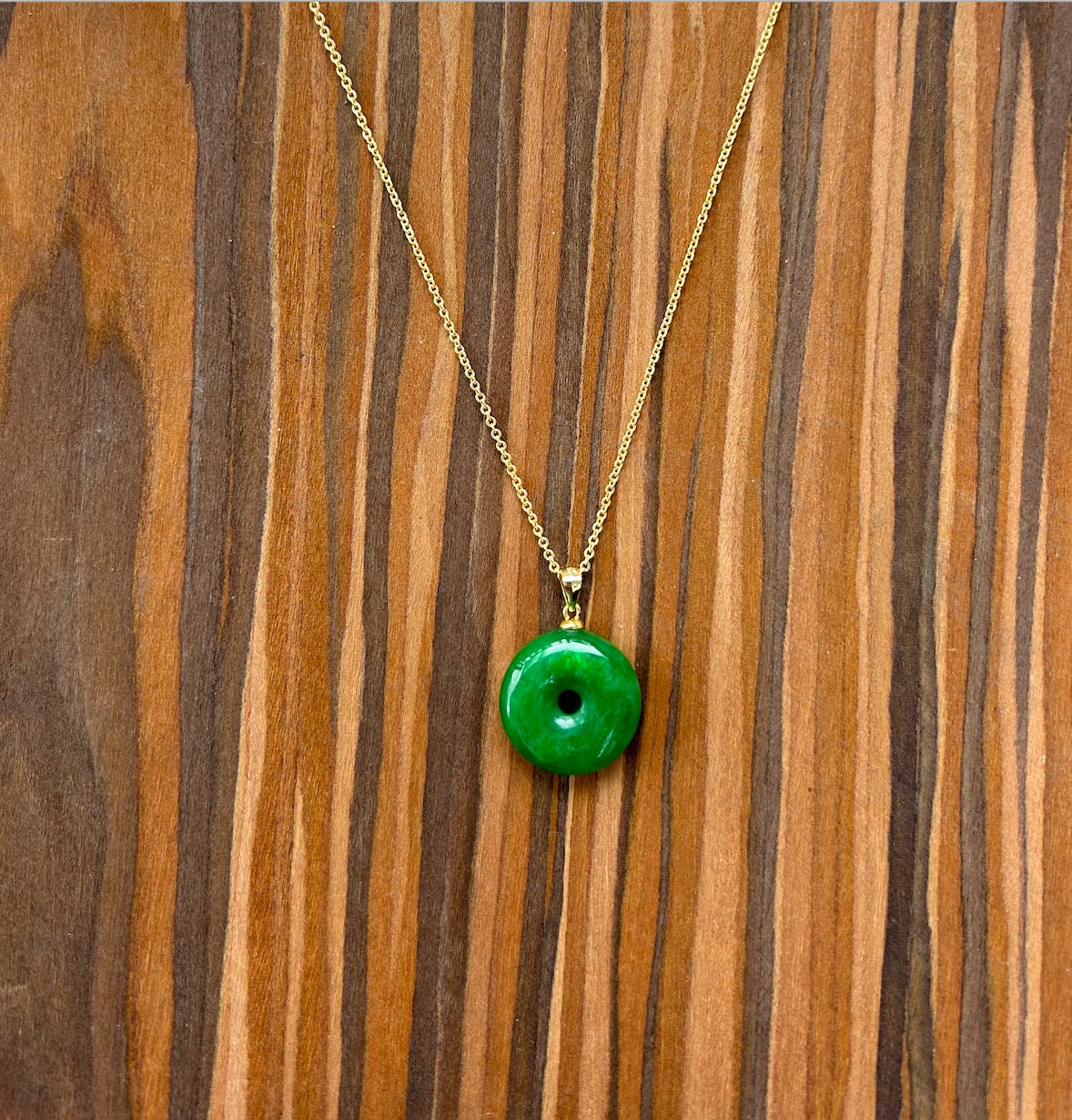 Front view of minimalist green jade donut necklace with 18k gold chain on wooden table