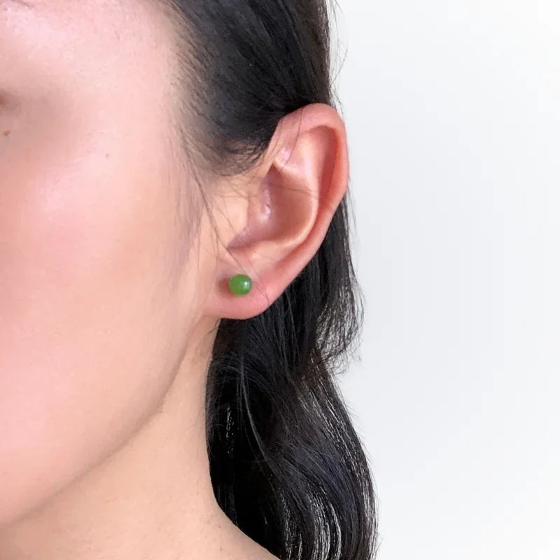 Close-up of an ear wearing a green earring against a white background