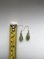 Green teardrop earrings next to a tape measure on a gray background