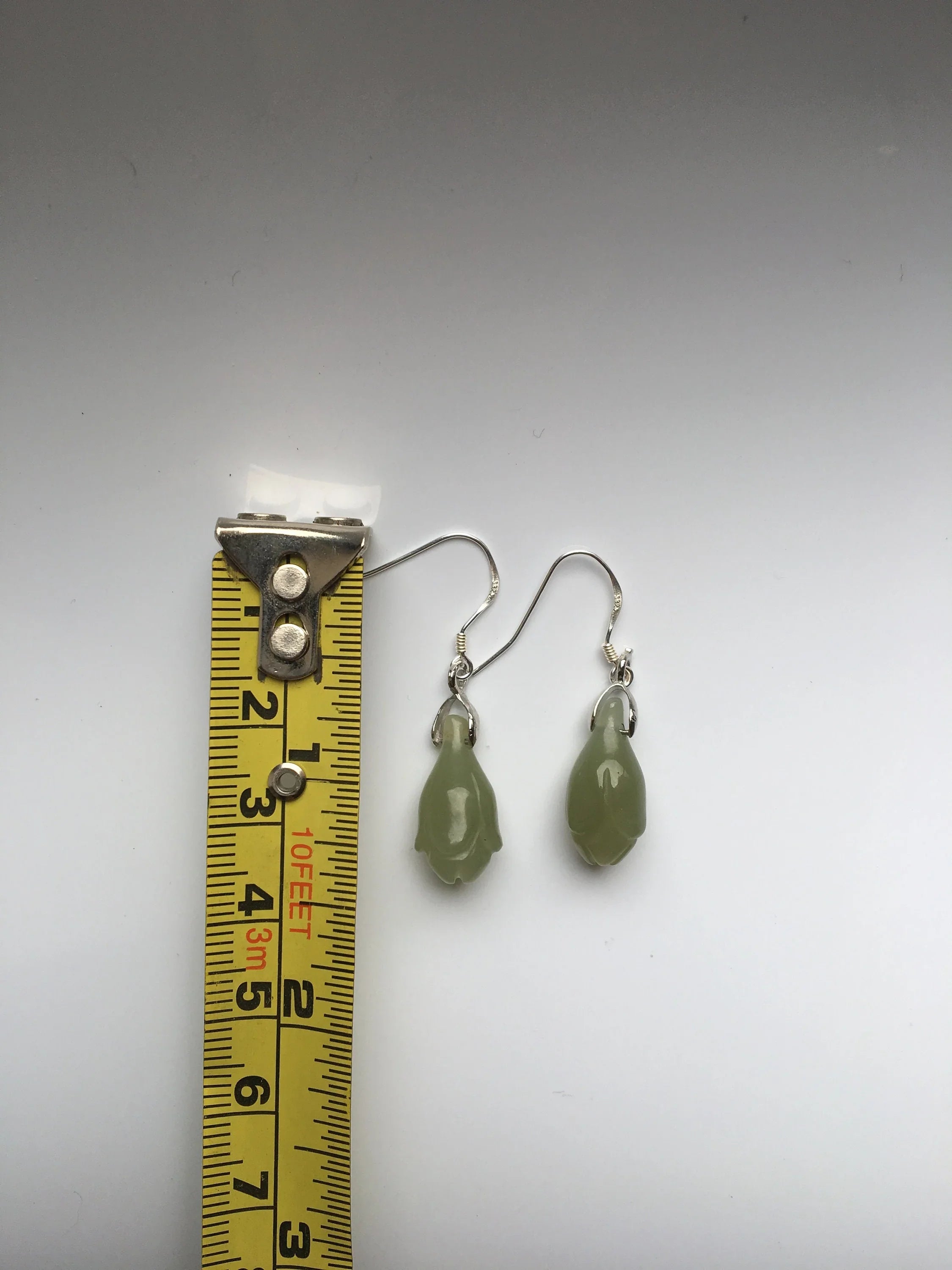 Green teardrop earrings next to a tape measure on a gray background