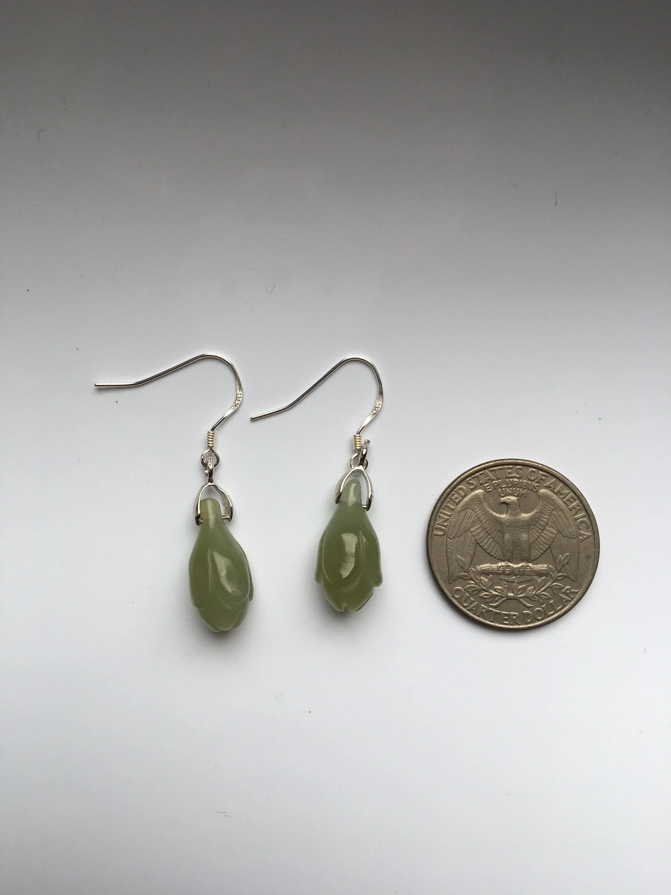 Green teardrop earrings next to a quarter on a white background