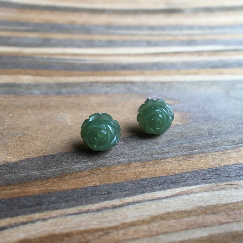 Front view of green jade rose stud earrings on woodgrain background