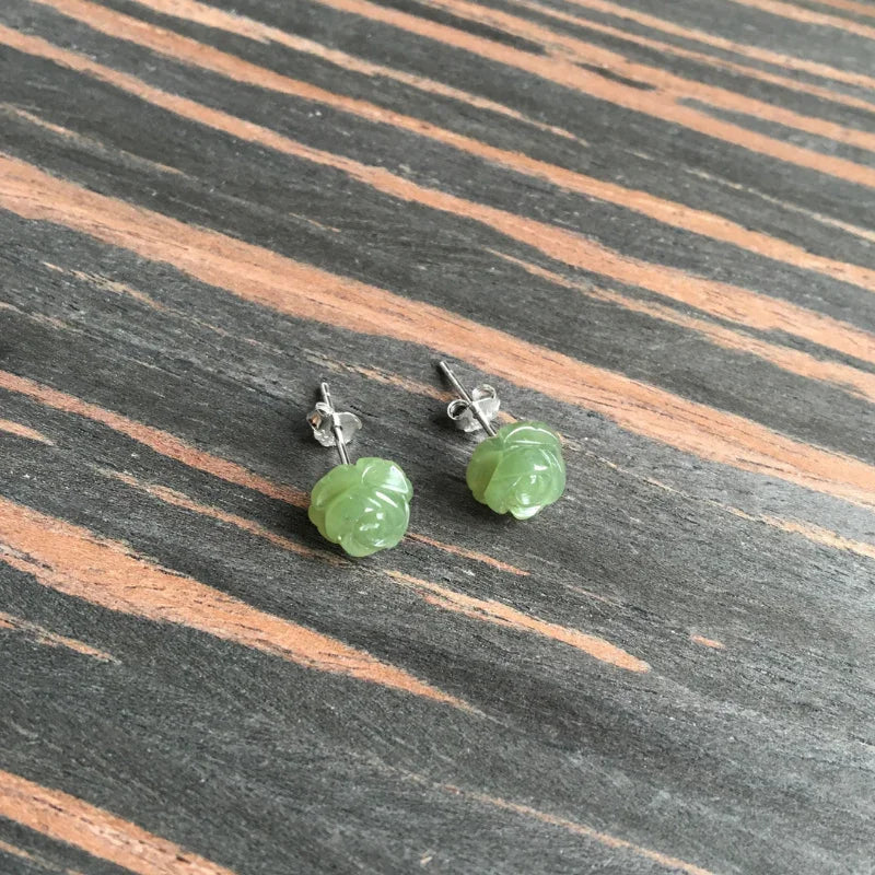 Green jade rose earrings viewed from side to show depth and carving detail of floral studs on wood background