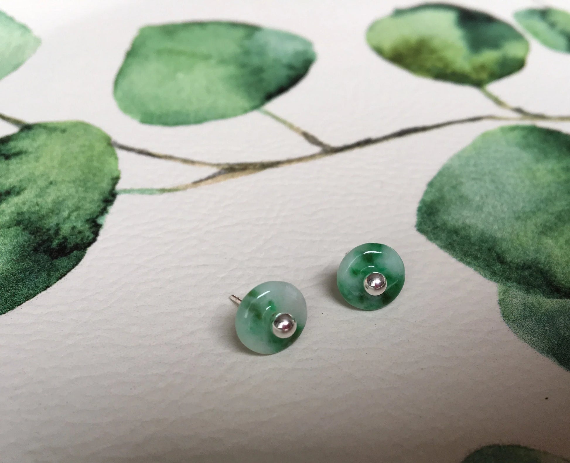 Green jade earrings on a white surface with green leaf pattern