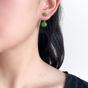 Close-up of a person wearing green bead earrings with a plain background