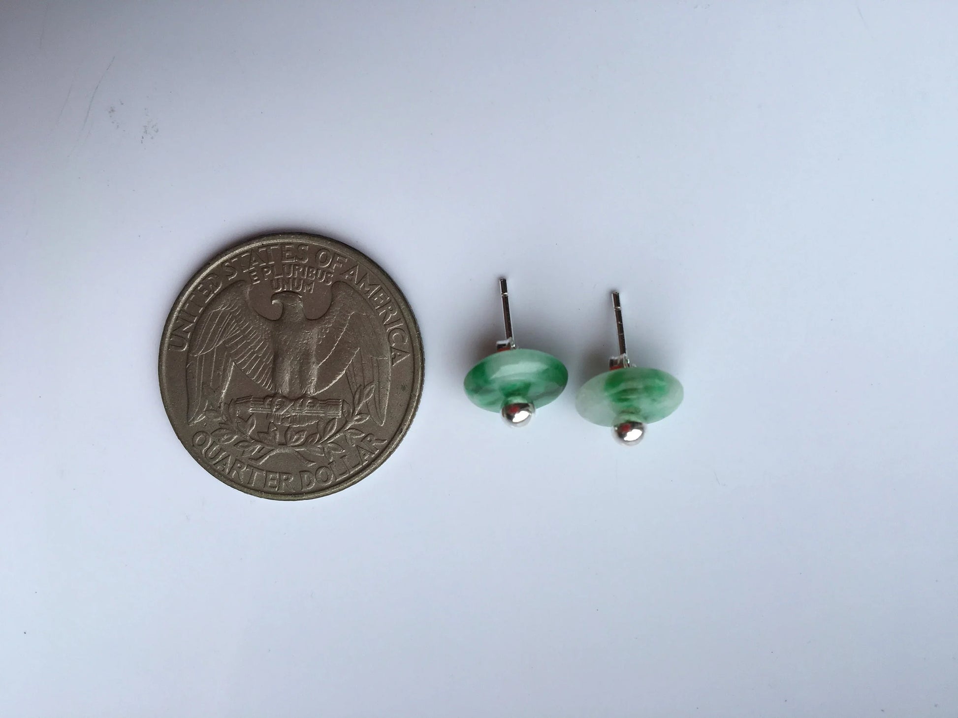 Green earrings next to a quarter on a white background