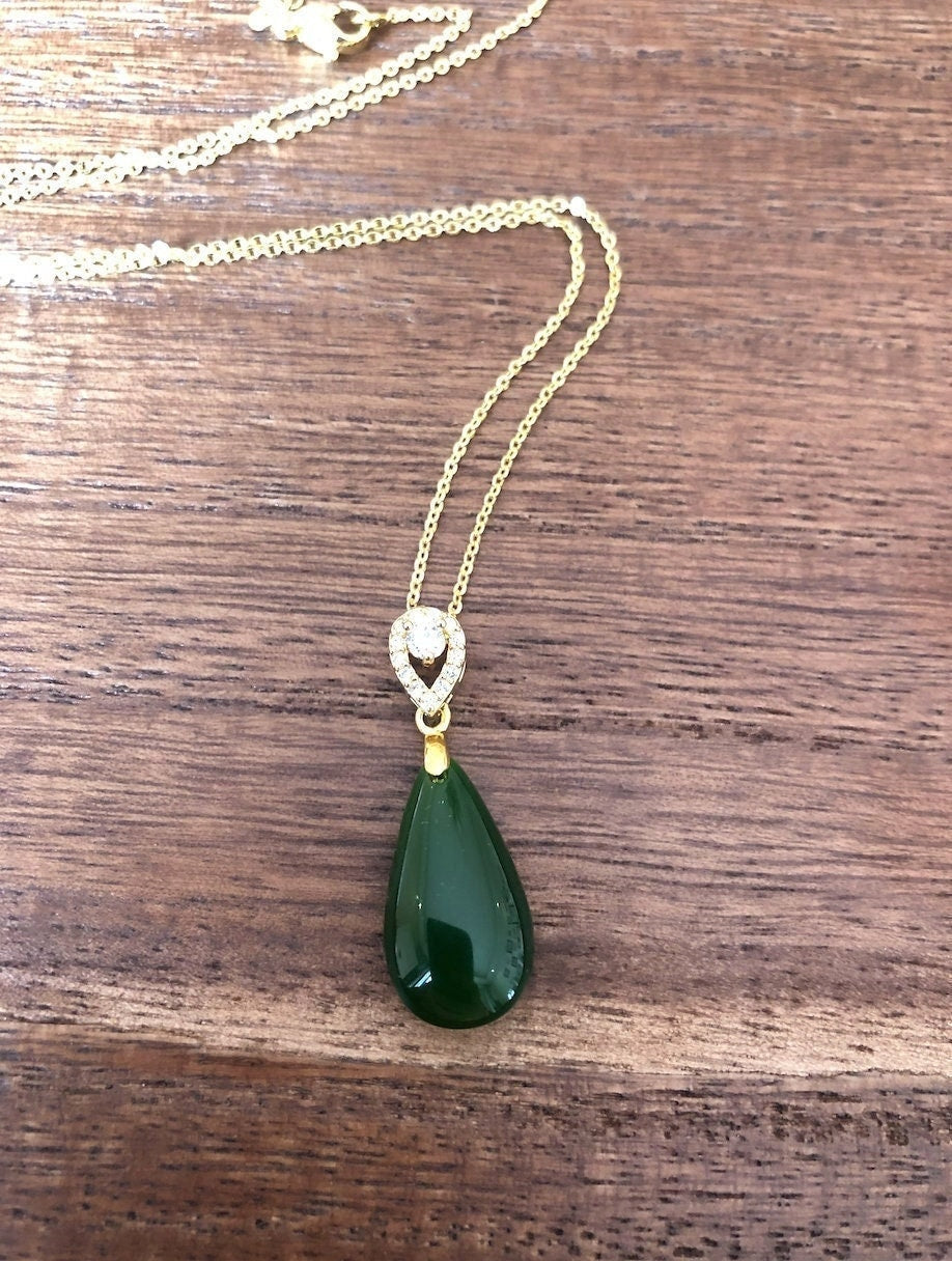 Green jade teardrop pendant necklace on gold chain, front view on wood background